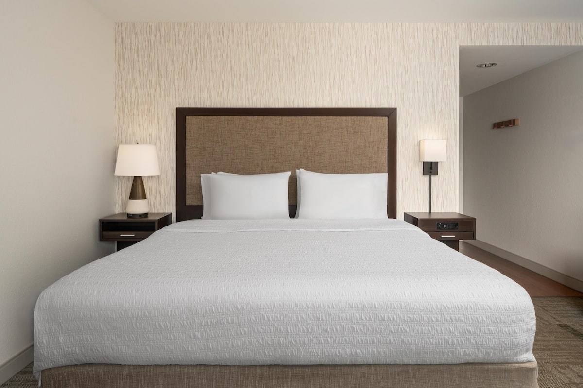A large bed with a wooden headboard, two bedside tables with lamps, and a textured wall.