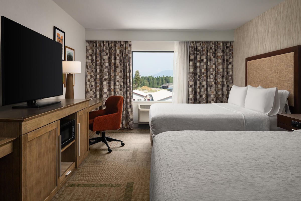 A hotel room with a large bed, a desk with a TV, a chair, and a window with curtains.