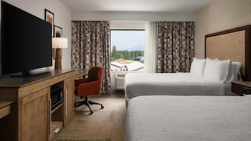A hotel room with a large bed, a desk with a TV, a chair, and a window with curtains.