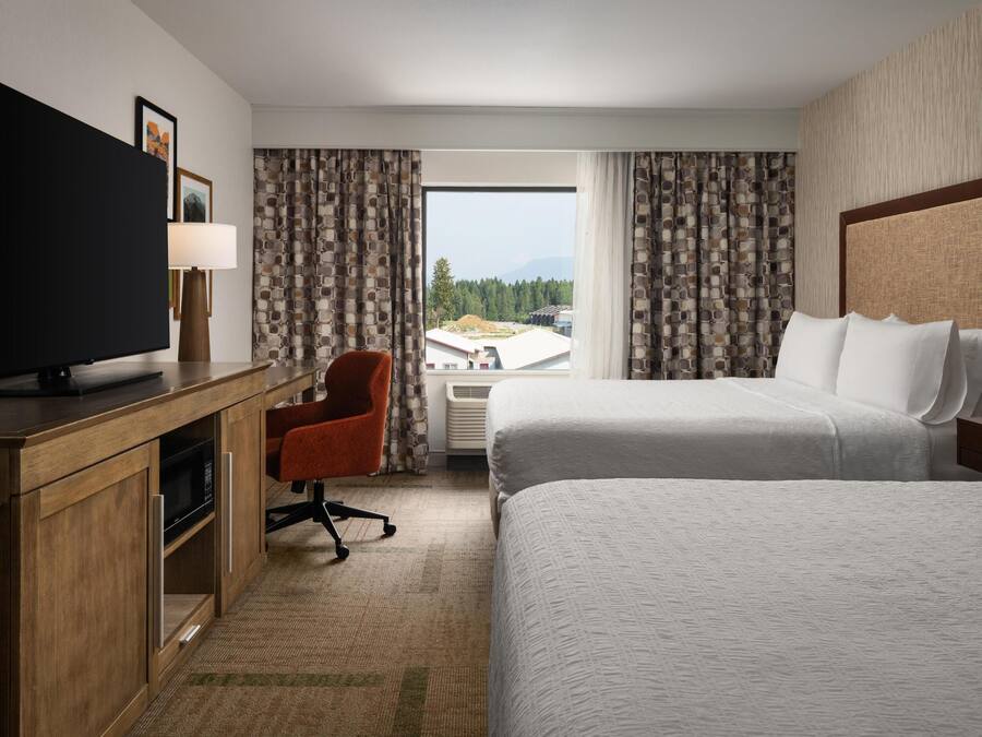 A hotel room with a large bed, a desk with a TV, a chair, and a window with curtains.