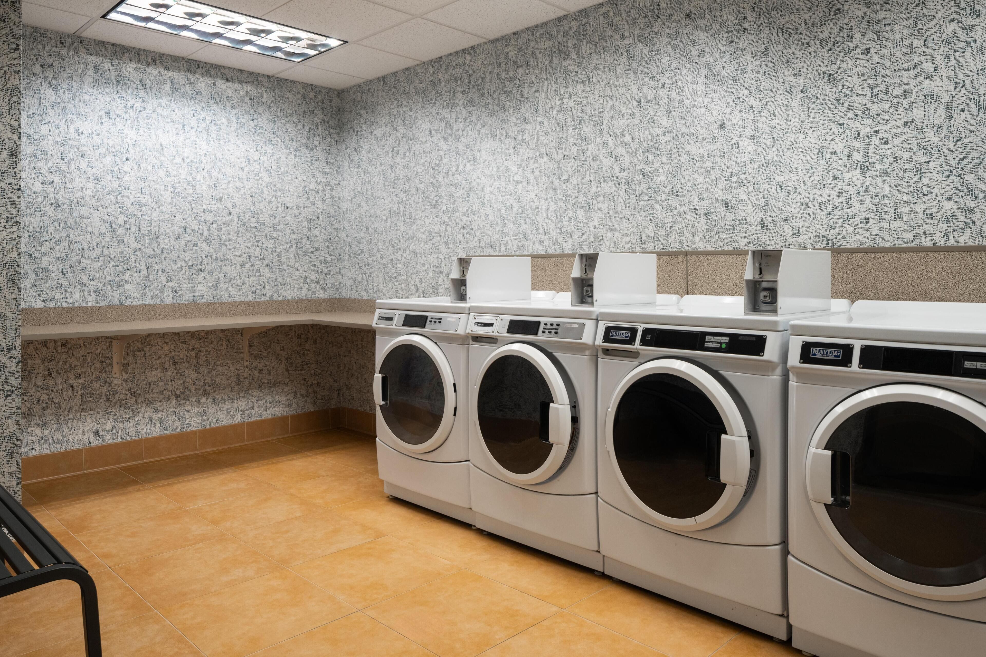 A laundry area with three front-loading washing machines, a bench, and a tiled floor.