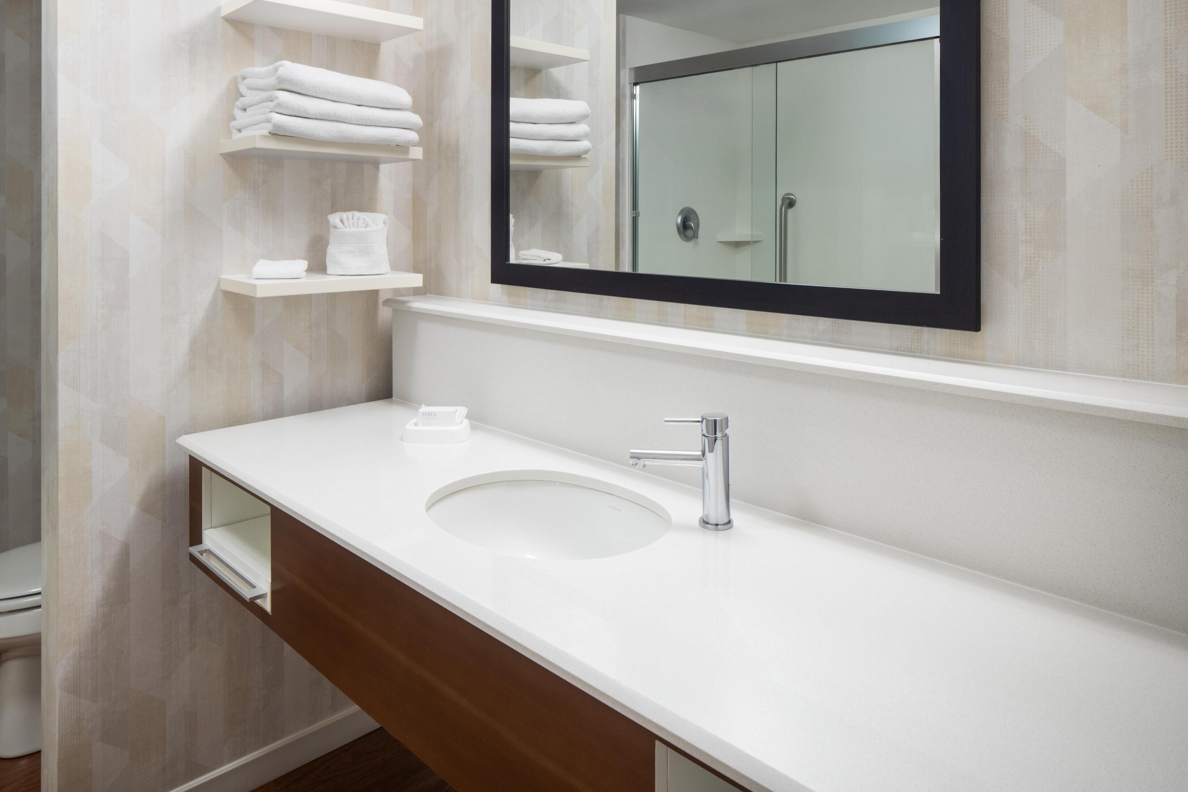 Une salle de bain avec un lavabo blanc, un miroir et des étagères où sont rangées des serviettes pliées.
