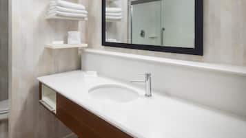 A bathroom with a white sink, a mirror, and shelves holding folded towels.