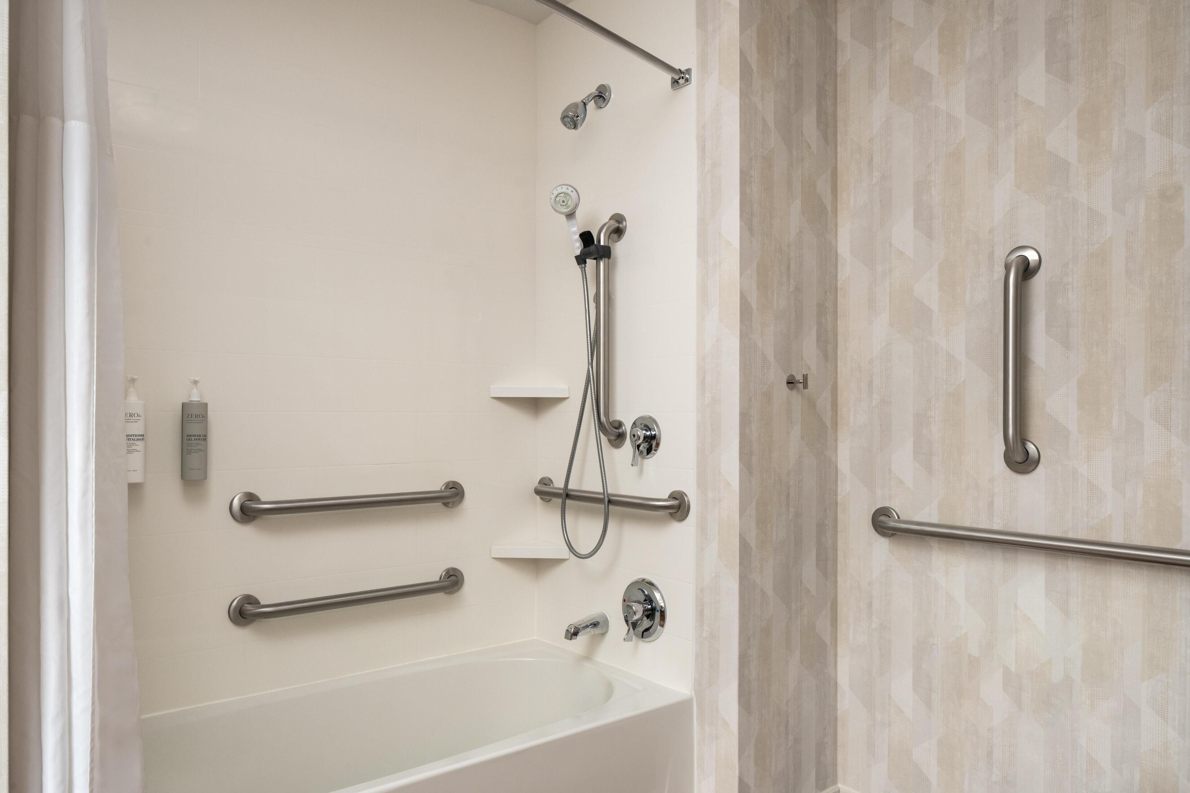 A bathroom with a bathtub, a shower with a handheld showerhead, and grab bars.