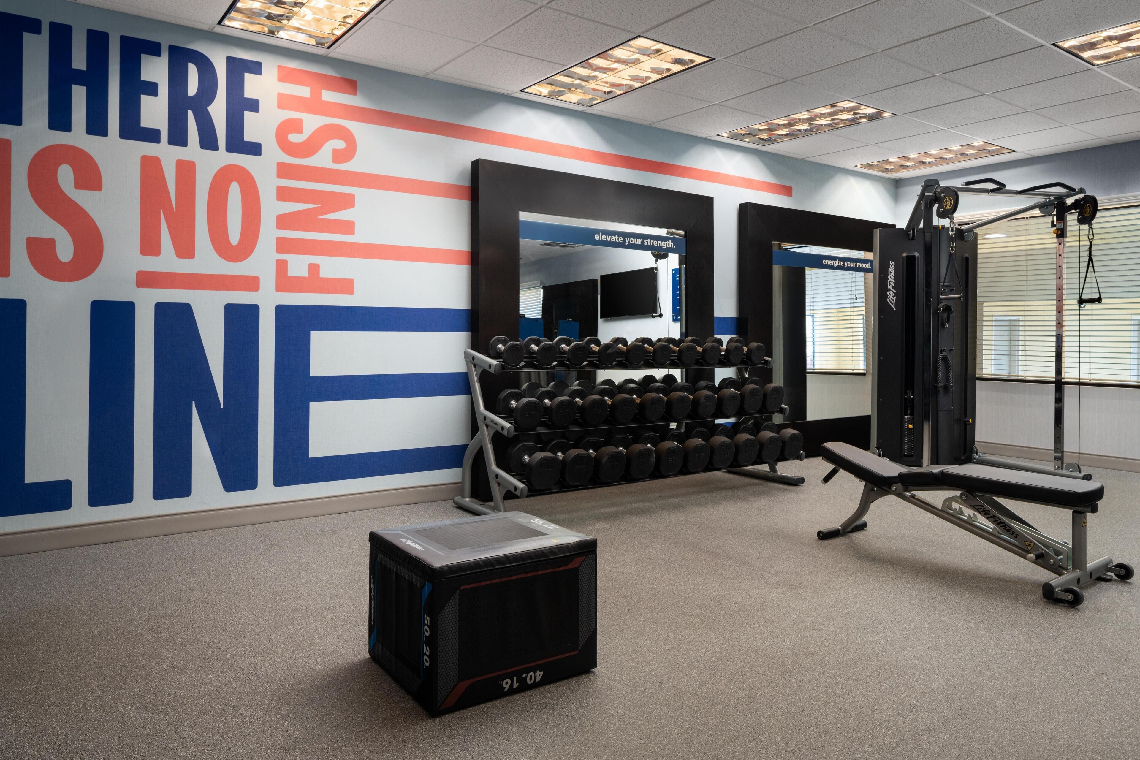 A gym with weightlifting equipment, a bench, and a motivational wall.