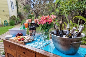 A wooden outdoor bar set with a variety of snacks, wine glasses, and bottles in a bucket.