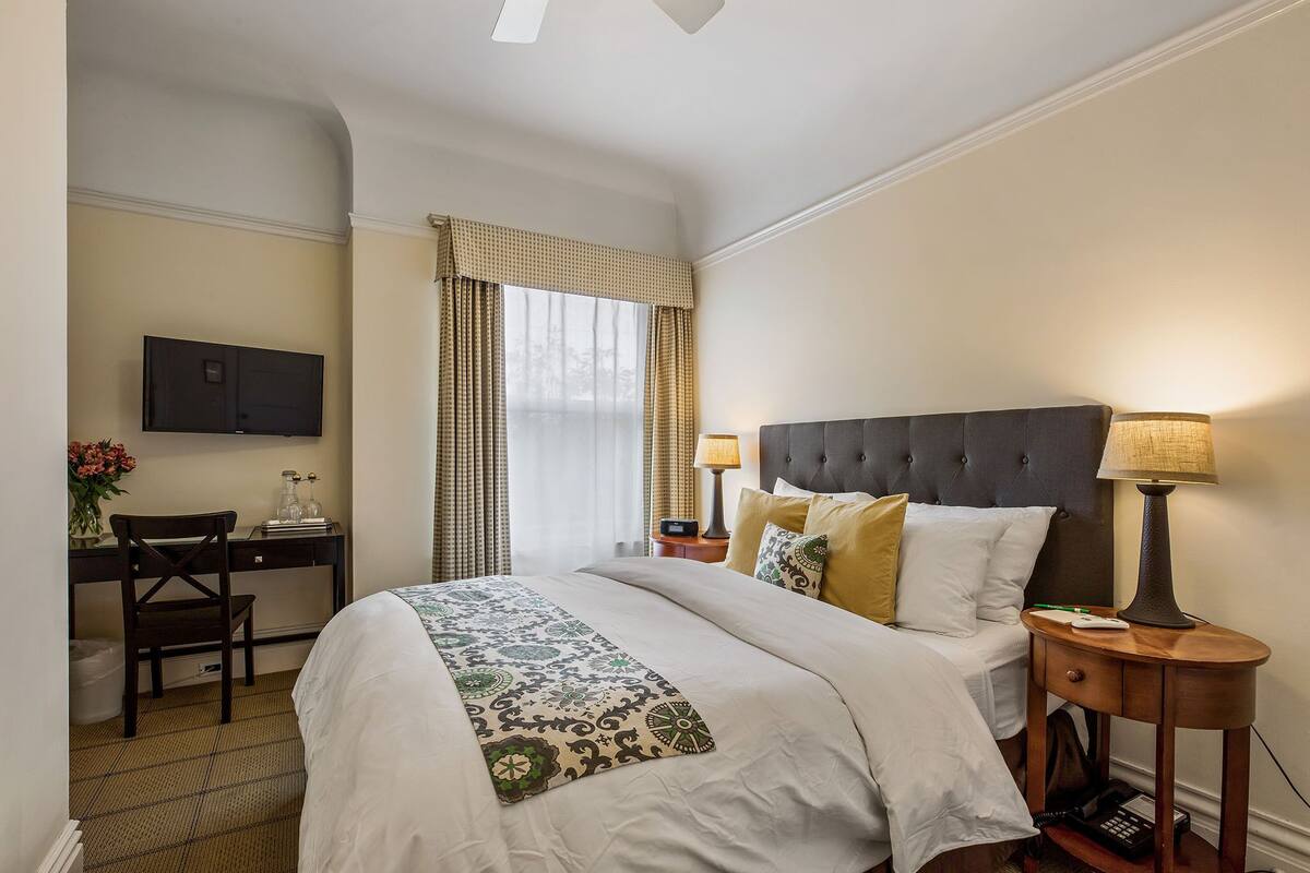Una camera d'albergo con un letto, abat-jour, una scrivania con televisore e una sedia.