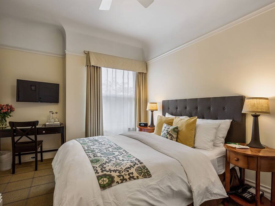Una habitación de hotel con cama, lámparas de noche, un escritorio con televisor y una silla.