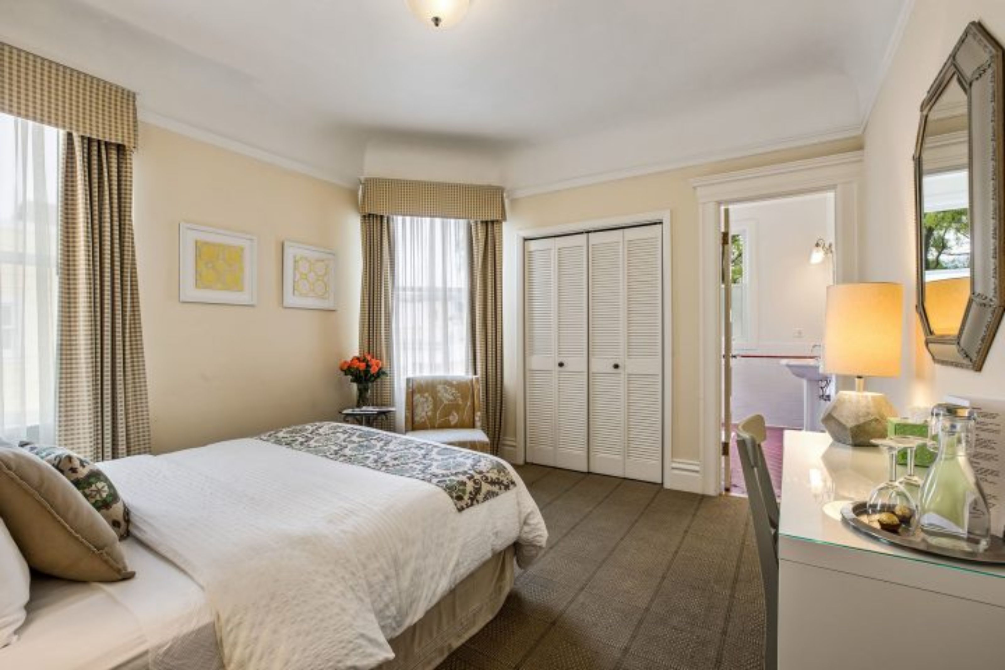 A hotel room with a large bed, a desk with a lamp, a mirror, and a wardrobe.