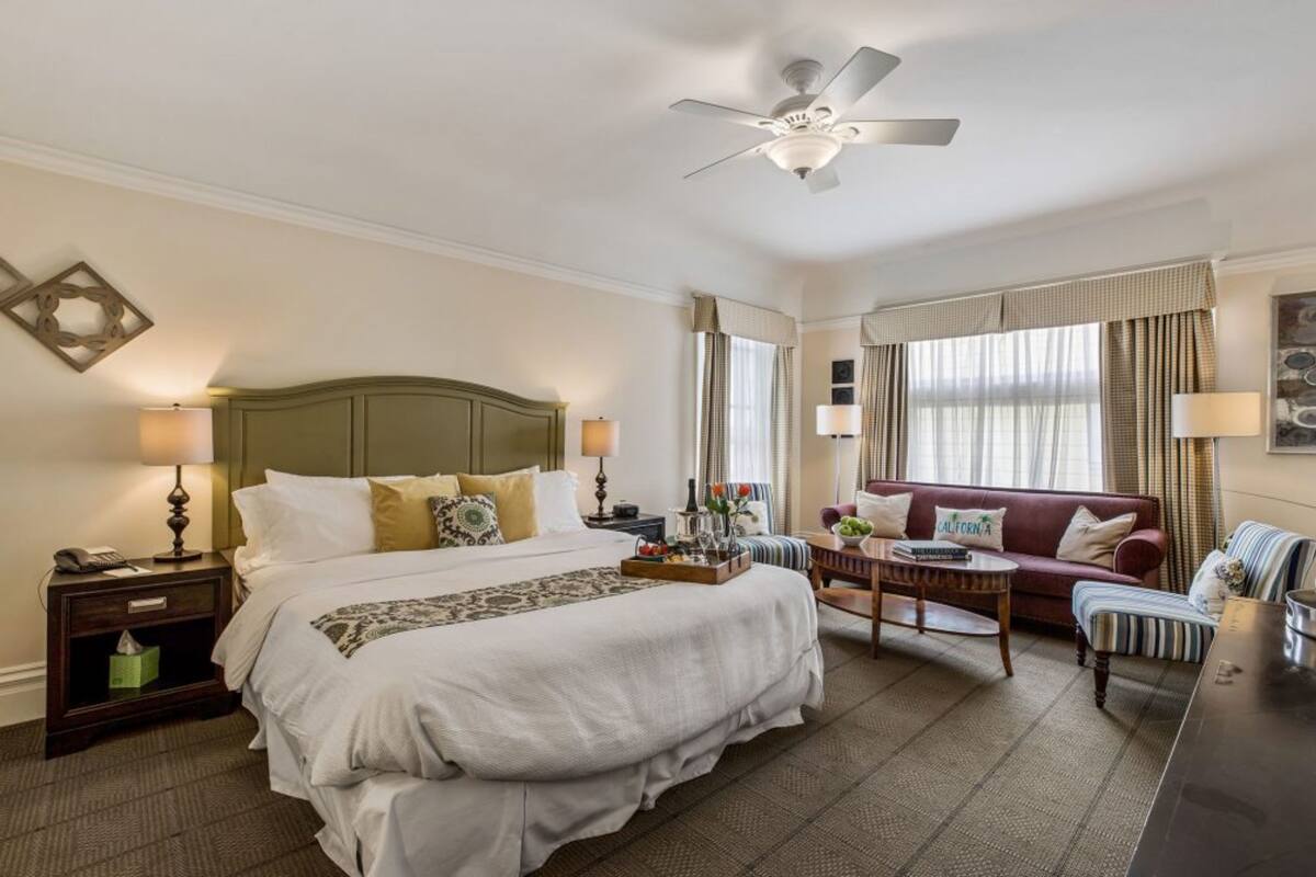 Una camera d'albergo con un letto grande, una scrivania, un divano e una ventola a soffitto.