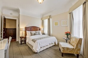 Ett hotellrum med en stor säng, ett nattduksbord med en lampa, en stol och ett litet bord med en vas med blommor.