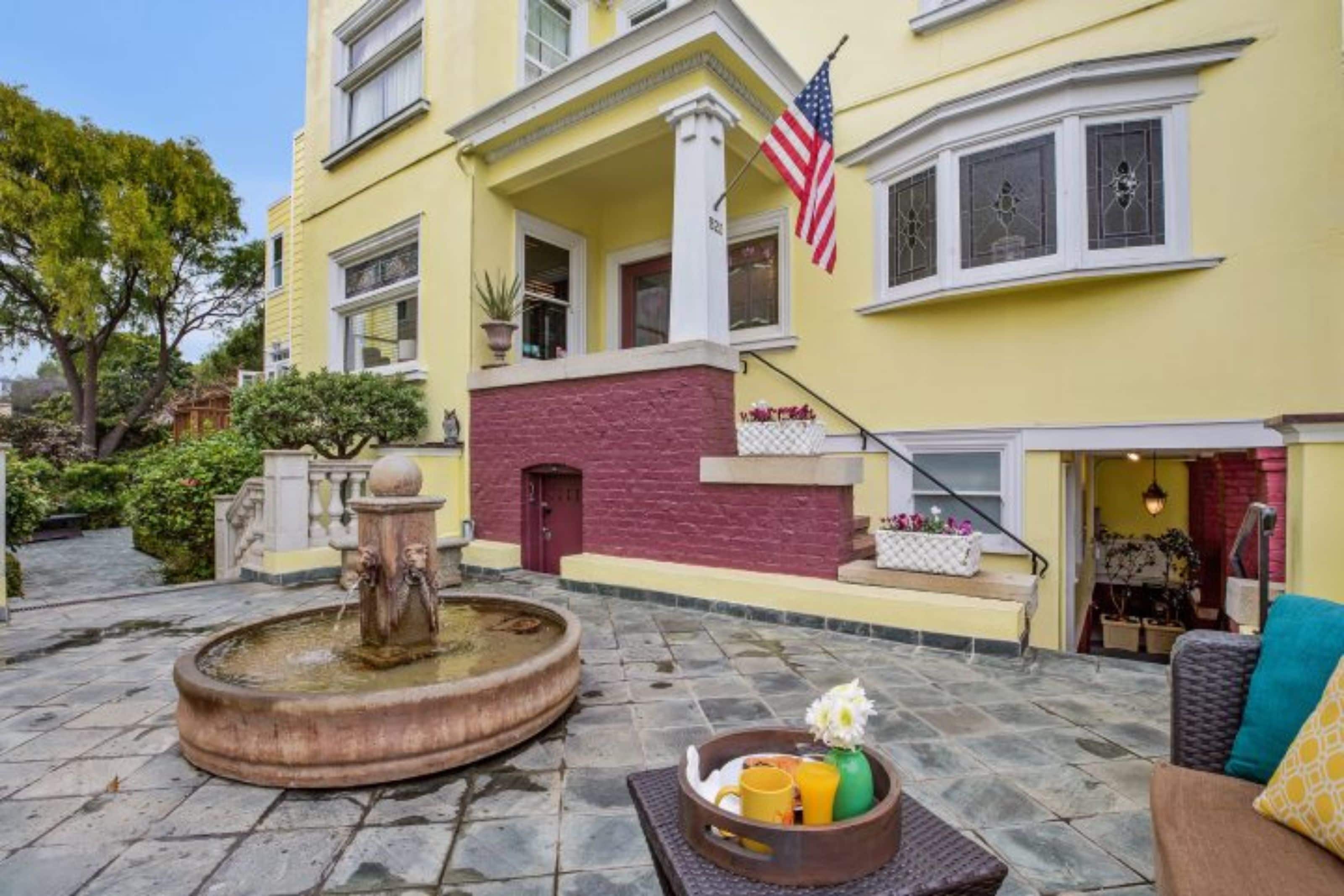 A yellow building with a fountain, a flag, and a tray of fruits and flowers.