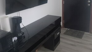 A modern living room with a flat-screen TV mounted on the wall, a coffee maker on a black console table, and a closed door.