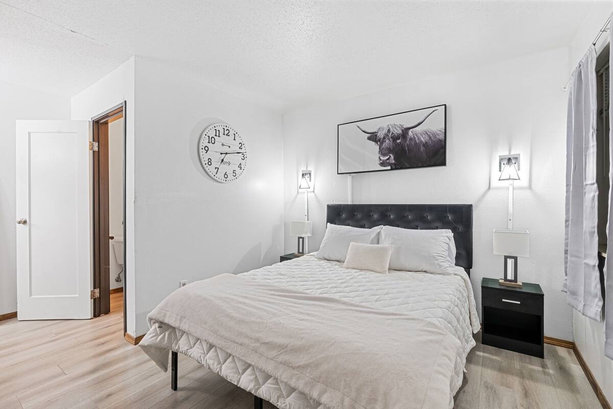 A bedroom with a bed, a clock, a framed picture, and two bedside lamps.