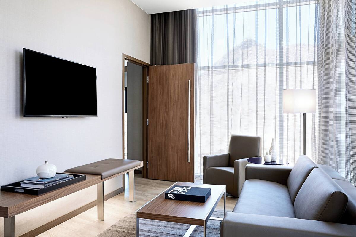 A modern hotel room with a flat-screen TV, a wooden bench, a sofa, and a coffee table.