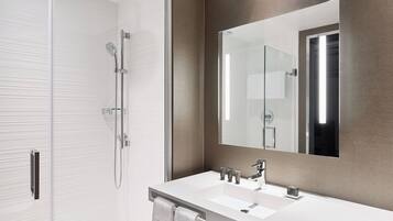 A modern bathroom with a glass shower enclosure, a white sink with a large mirror, and a towel rack.