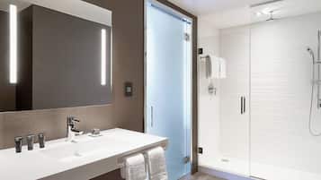 A modern bathroom with a large mirror, a white sink, and a glass-enclosed shower.