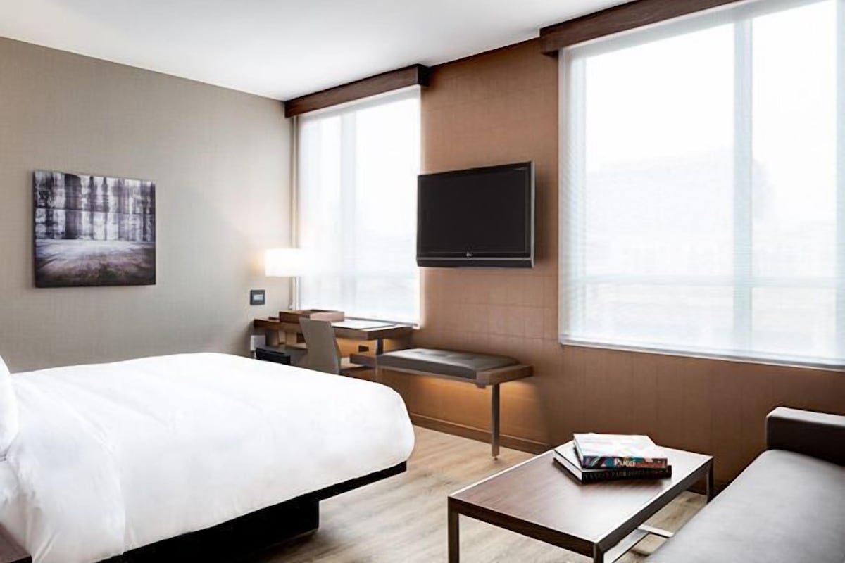 A hotel room with a bed, a desk, a TV, and a window.