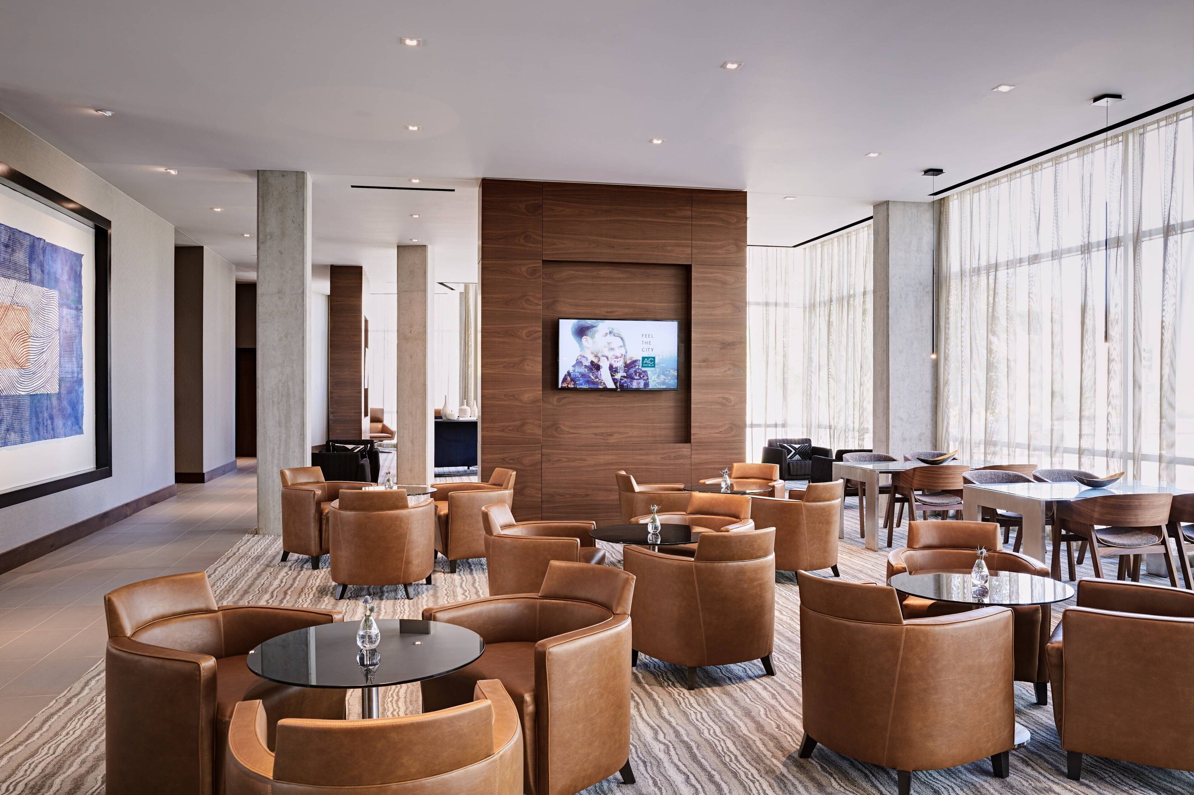 A modern hotel lobby with leather seating, a large TV screen, and large windows.