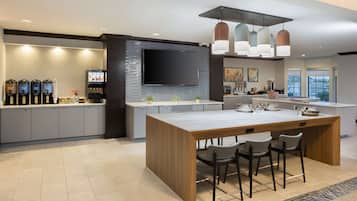 Una cocina moderna con una isla central, taburetes de bar, un televisor de pantalla plana y una estación de café.
