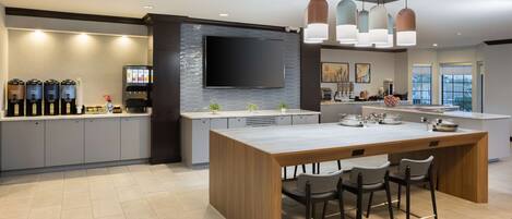 A modern kitchen with a central island, bar stools, a flat-screen TV, and a coffee station.