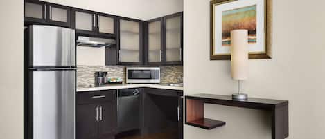 Una cocina moderna con gabinetes oscuros, electrodomésticos de acero inoxidable, un microondas y un cuadro en la pared.