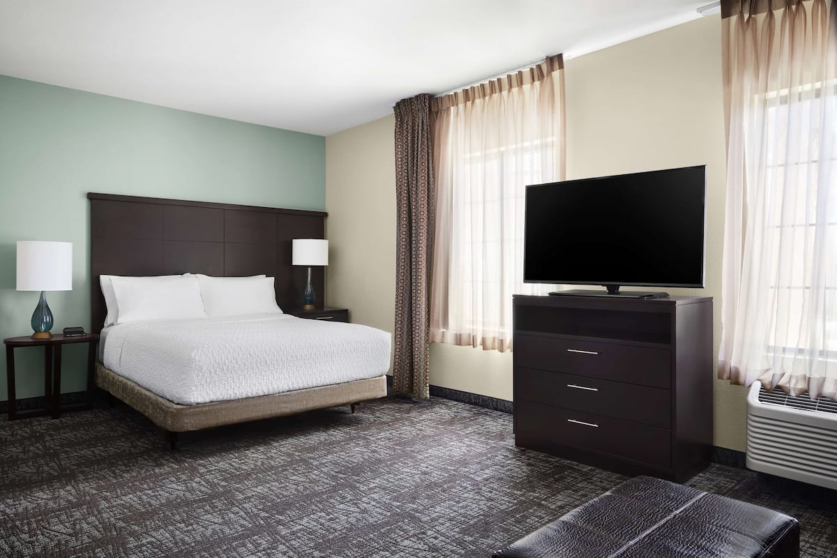 Une chambre d’hôtel comprenant un lit, des tables de chevet, un téléviseur à écran plat, une commode et une fenêtre avec des rideaux.