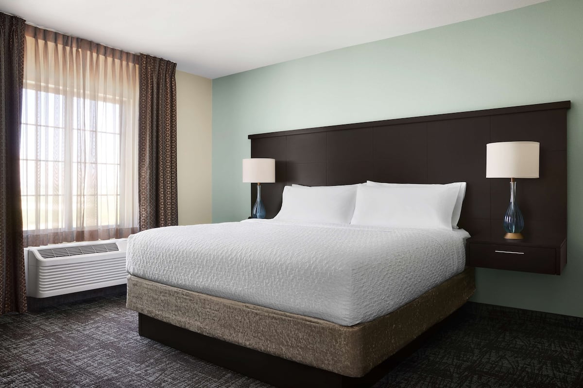 Une chambre d’hôtel avec un grand lit, deux lampes de chevet, une fenêtre avec des rideaux et un climatiseur fixé au mur.