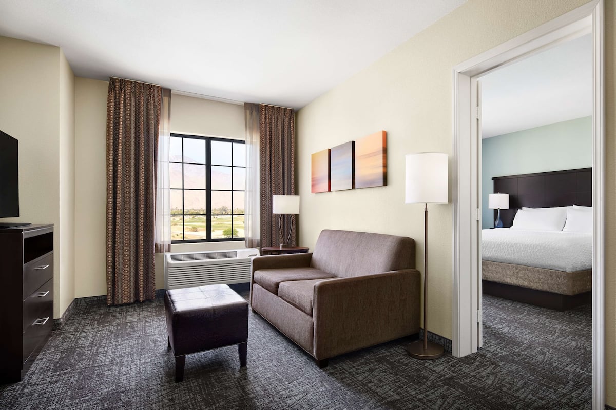 Une chambre d’hôtel avec un canapé, une petite table, une télévision, un lit et une fenêtre avec des rideaux.