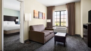 Een hotelkamer met een bed, een bank, een salontafel, een televisie en een raam met gordijnen.