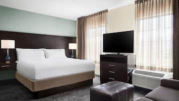 Une chambre d’hôtel avec un grand lit, deux lampes de chevet, un téléviseur à écran plat, un radiateur et une fenêtre avec des rideaux légers.