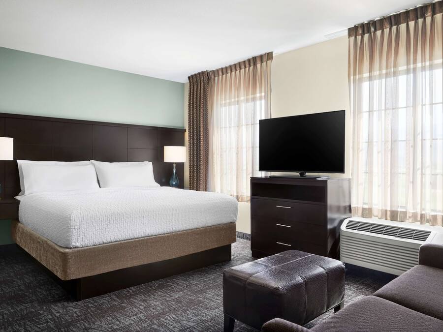 Une chambre d’hôtel avec un grand lit, deux lampes de chevet, un téléviseur à écran plat, un radiateur et une fenêtre avec des rideaux légers.