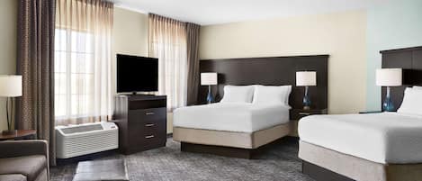 A hotel room with a large bed, two bedside tables with lamps, a flat-screen TV, a heater, and a small seating area.