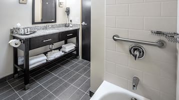 A modern bathroom with a granite countertop sink, a mirror, a towel rack, and a shower with a grab bar.