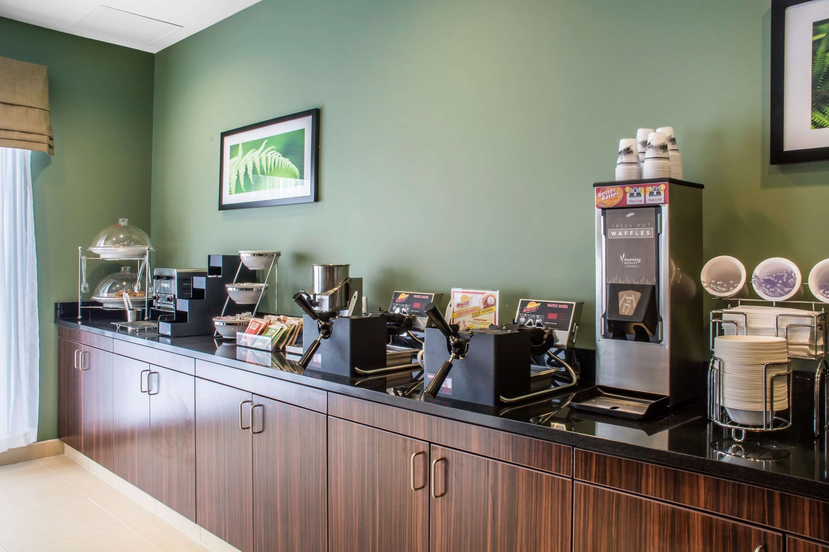 A coffee station with multiple coffee machines, a waffle maker, and a stack of white plates.
