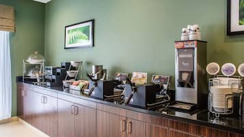 A coffee station with multiple coffee machines, a waffle maker, and a stack of white plates.