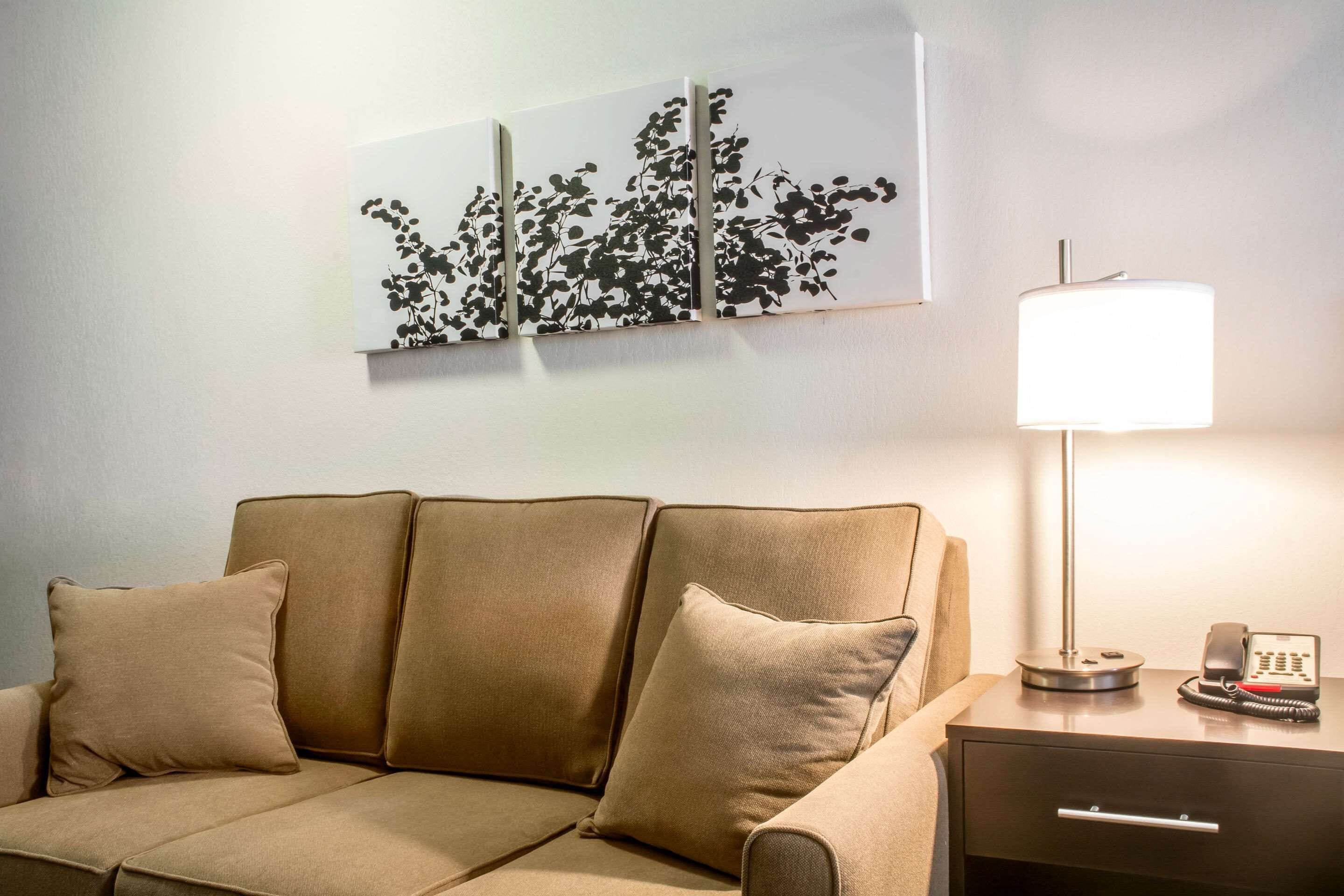 A hotel room with a beige sofa, a bedside table with a lamp and phone, and a wall-mounted artwork.