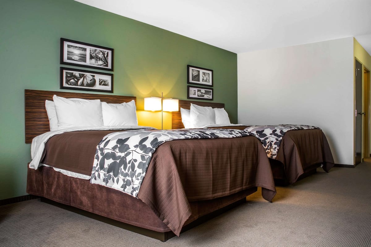 Habitación de hotel con dos camas, cabecero de madera, pared verde y cuadros enmarcados.