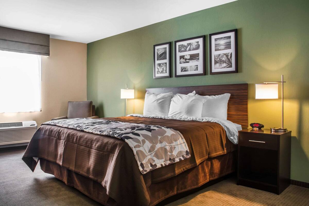 Una habitación de hotel con una cama grande, dos lámparas de noche, una mesita de noche y un cuadro enmarcado sobre la cama.