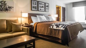 A hotel room with a bed, a sofa, a nightstand, and a lamp. - Sleep Inn & Suites Syracuse Airport (East Syracuse)