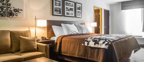 Une chambre d’hôtel avec un lit, un canapé, une table de chevet et une lampe.