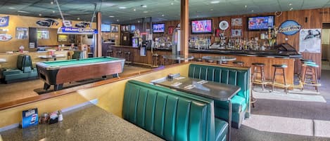 A bar area with green booths, a pool table, and multiple TVs on the wall.