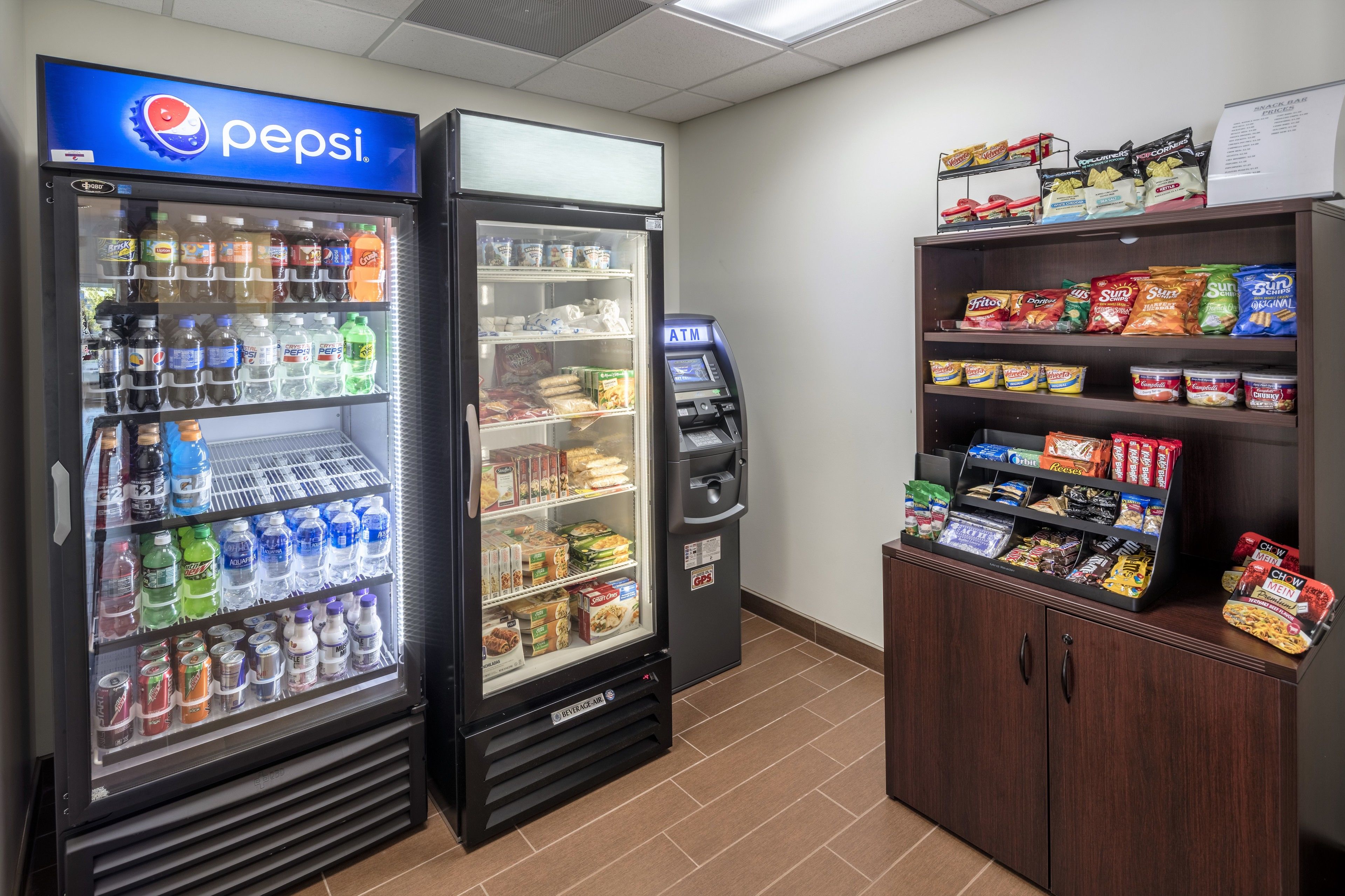 Ein Automatenbereich mit einem Pepsi-Kühler, einem Geldautomaten und Verkaufsregalen für Snacks.