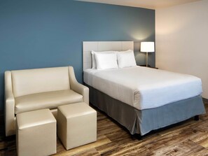 A hotel room with a bed, a sofa, and two ottomans.