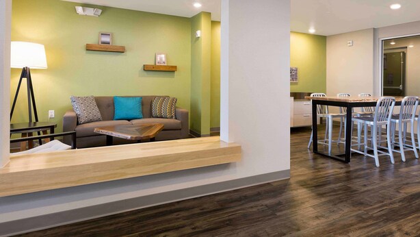 A modern living room with a sofa, a coffee table, and a dining area with chairs. - WoodSpring Suites Las Colinas - Northwest Dallas (Irving)