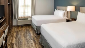 A hotel room with two beds, a TV, a desk, and a window with curtains. - WoodSpring Suites Las Colinas - Northwest Dallas (Irving)