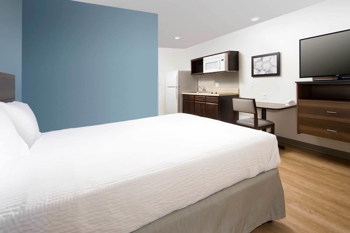 A hotel room with a bed, a desk, a chair, a TV, and a microwave.