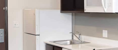 Una cocina compacta con un refrigerador blanco, un microondas sobre la encimera, un fregadero y un lavavajillas.