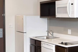 A compact kitchen with a white refrigerator, a microwave above the counter, a sink, and a dishwasher. - WoodSpring Suites Houston IAH Airport (Humble)