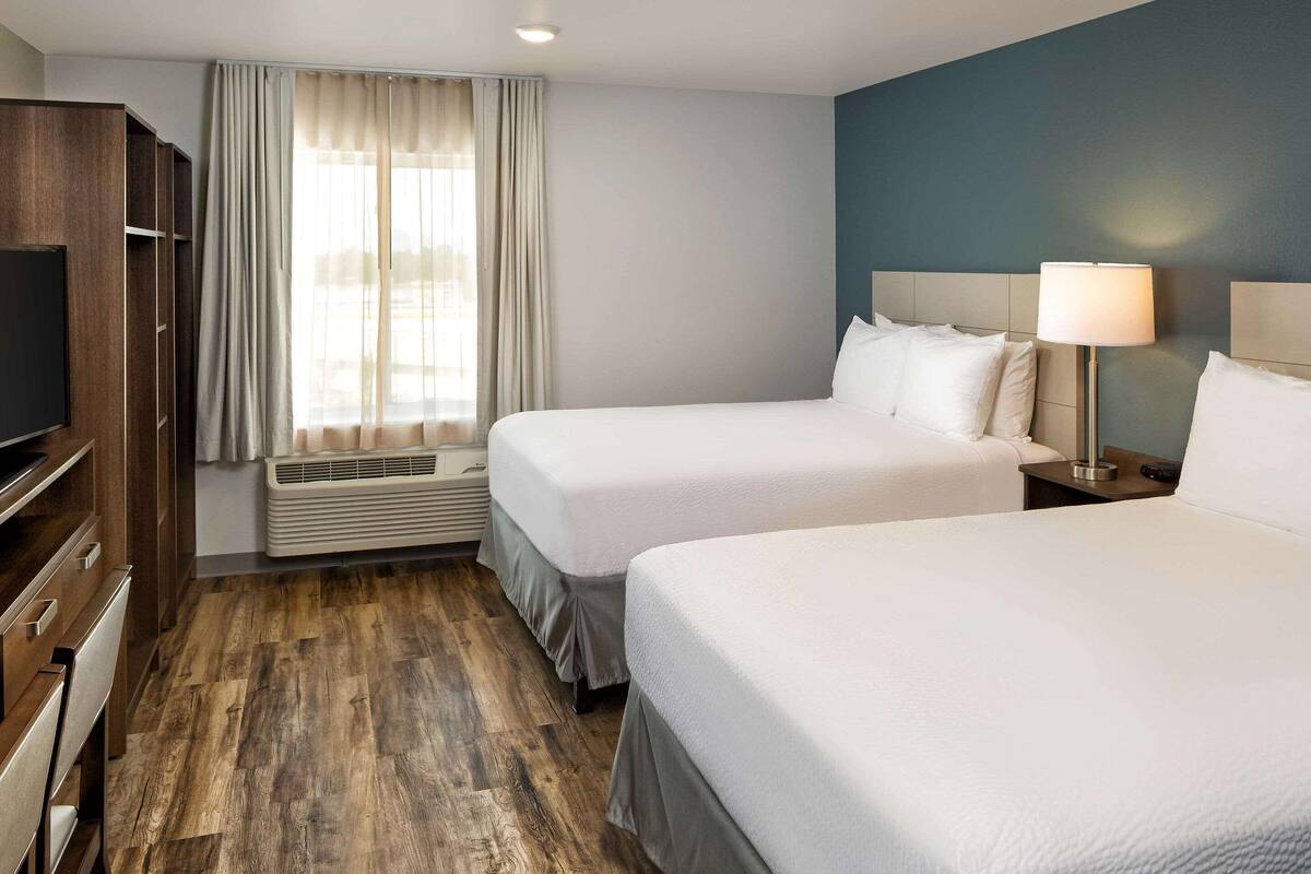 A hotel room with two beds, a TV, a wardrobe, and a window with curtains.